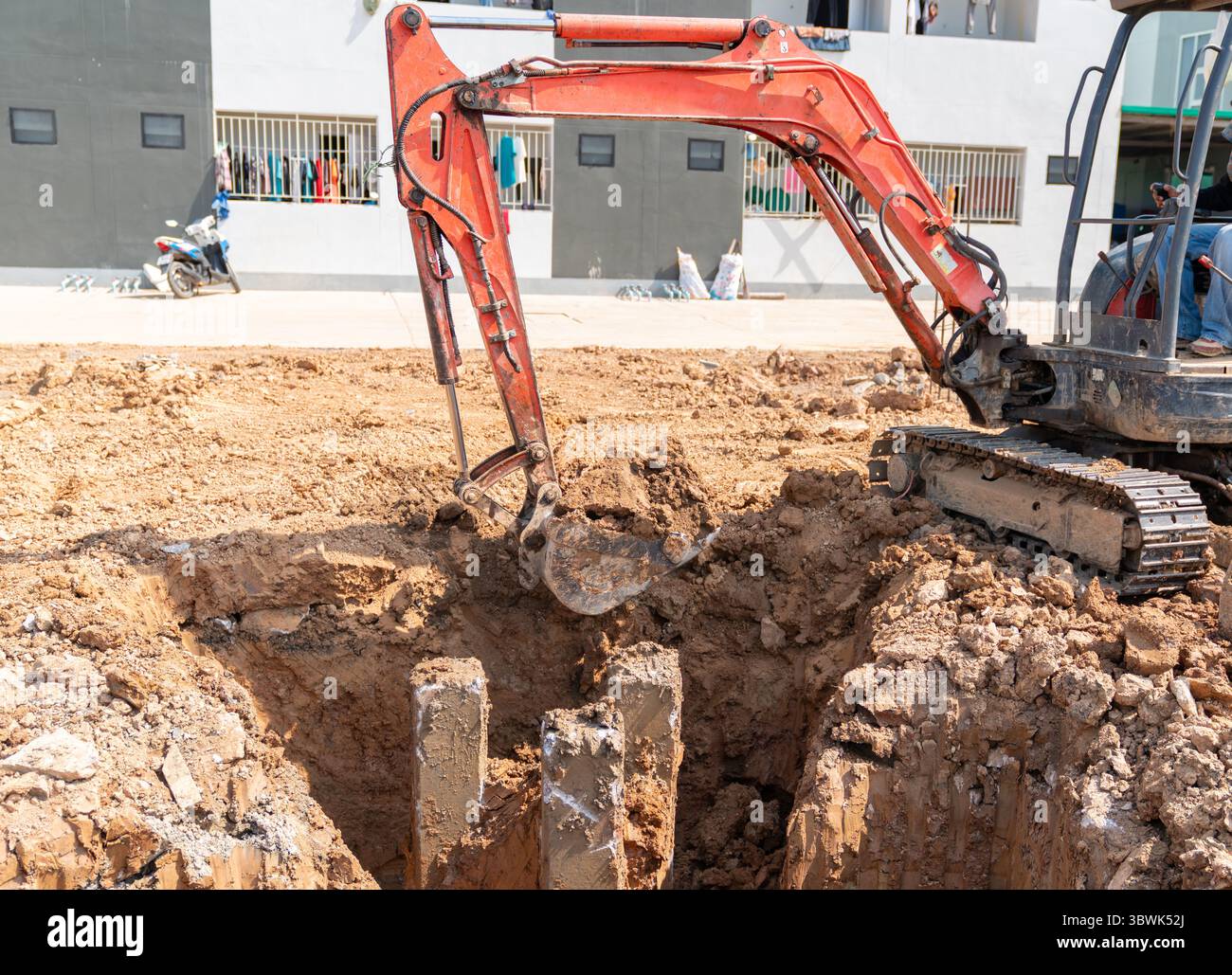 Une mini pelle excavatrice creuse le sol autour de la tête de pieu en préparation pour couler le chapeau de pieu. Banque D'Images