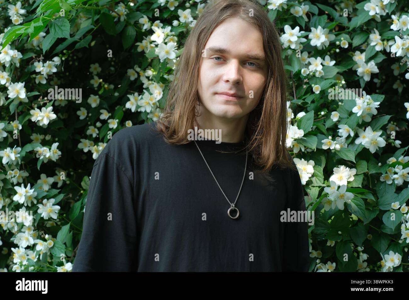 Un jeune homme se tient paisiblement au milieu de fleurs blanches vibrantes, profitant de la beauté de la nature. Banque D'Images