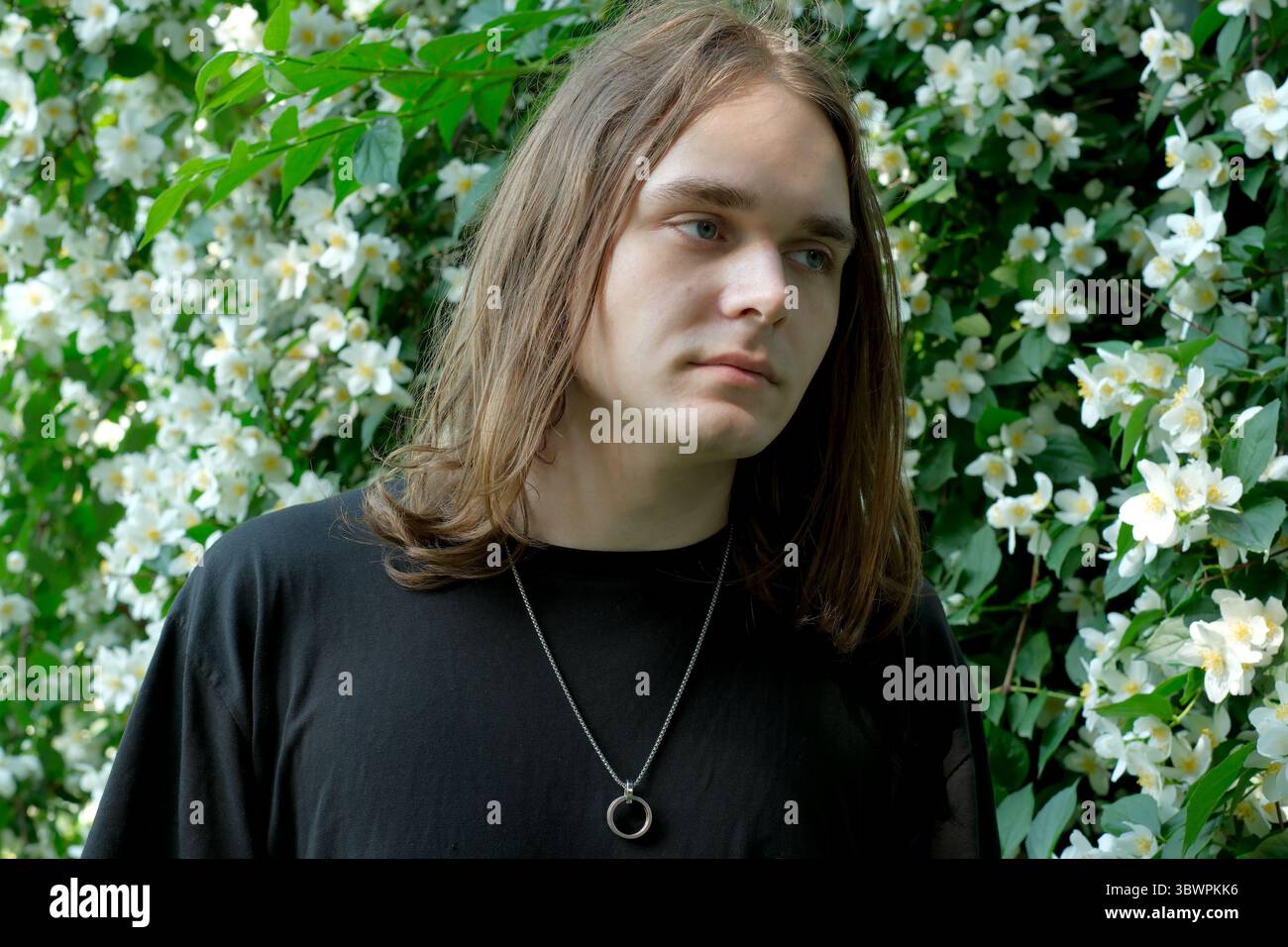 Un jeune homme aux cheveux longs se tient tranquillement au milieu de fleurs blanches vibrantes, dégageant le calme. Banque D'Images