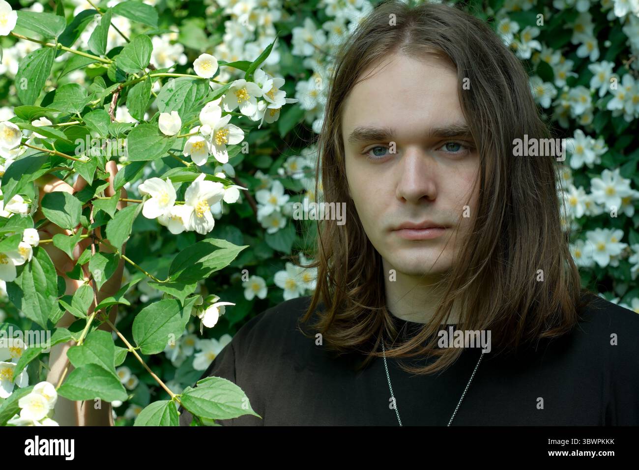 Un jeune homme se tient au milieu des fleurs blanches en cascade, profitant d'une journée ensoleillée à l'extérieur. Banque D'Images