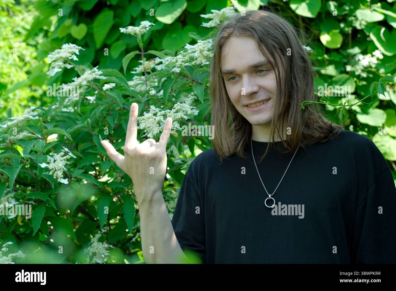 Au milieu d'une végétation luxuriante, un jeune homme clignote un geste de la main rempli de joie et d'énergie. Banque D'Images