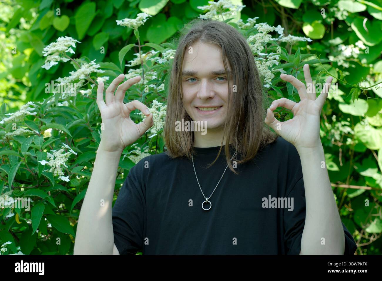 Une jeune joyeuse pose avec des signes à la main parmi un feuillage vert vibrant. Banque D'Images