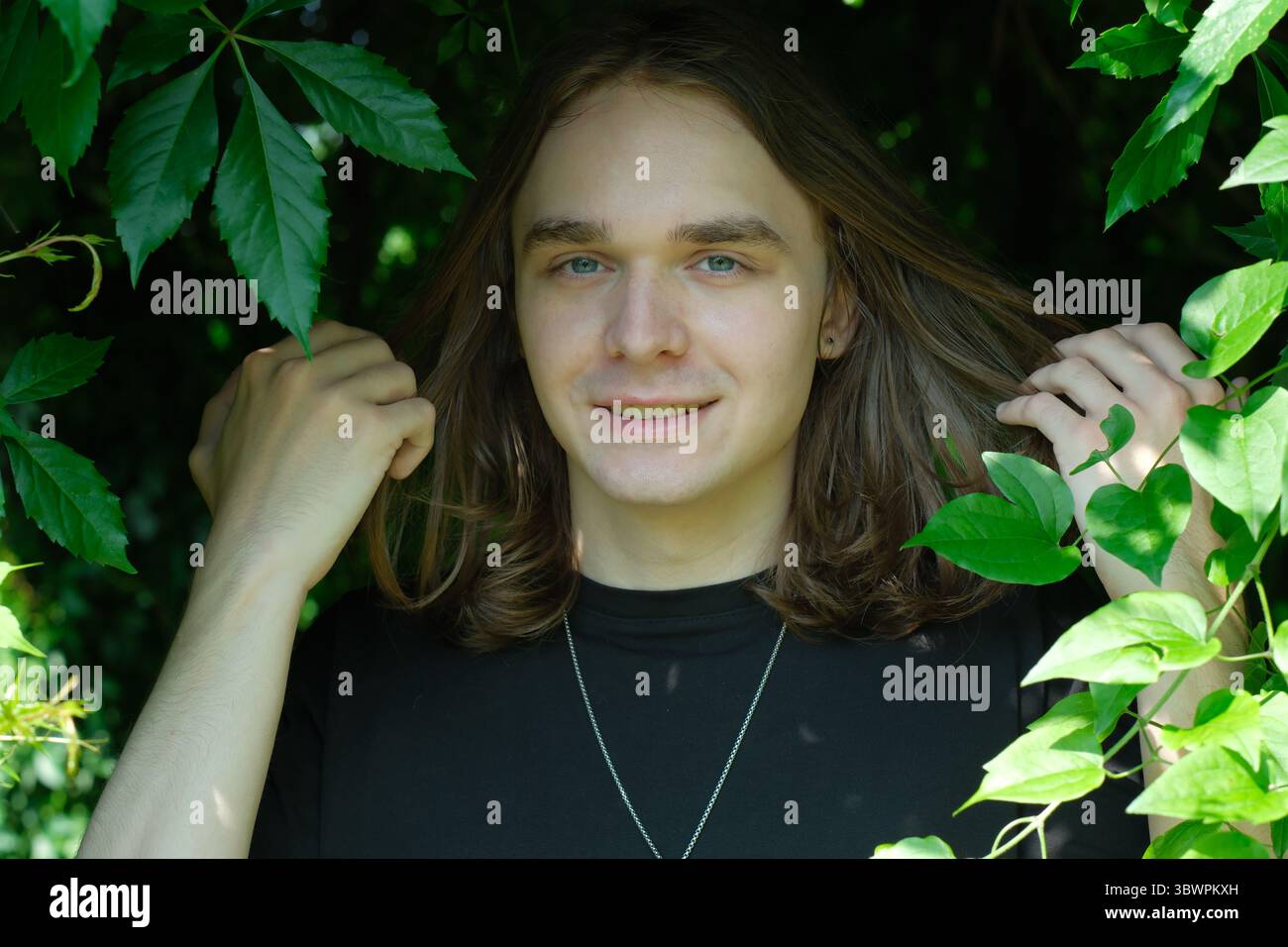 Un jeune adulte se tient dans un feuillage vibrant, exsudant le bonheur tout en touchant doucement les feuilles. Banque D'Images