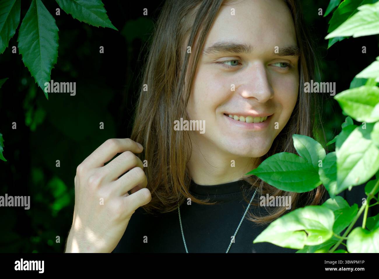 Une jeune personne aux cheveux longs sourit doucement tout en étant entourée d'une végétation luxuriante. Banque D'Images