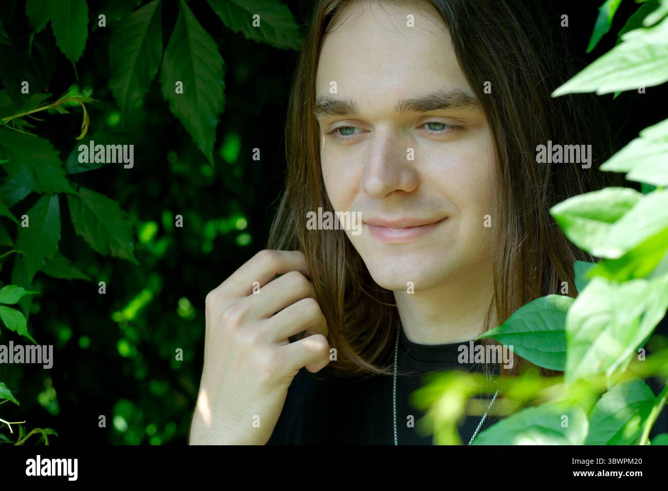 Un jeune homme aux cheveux longs profite d'un moment paisible entouré de feuilles vibrantes. Banque D'Images