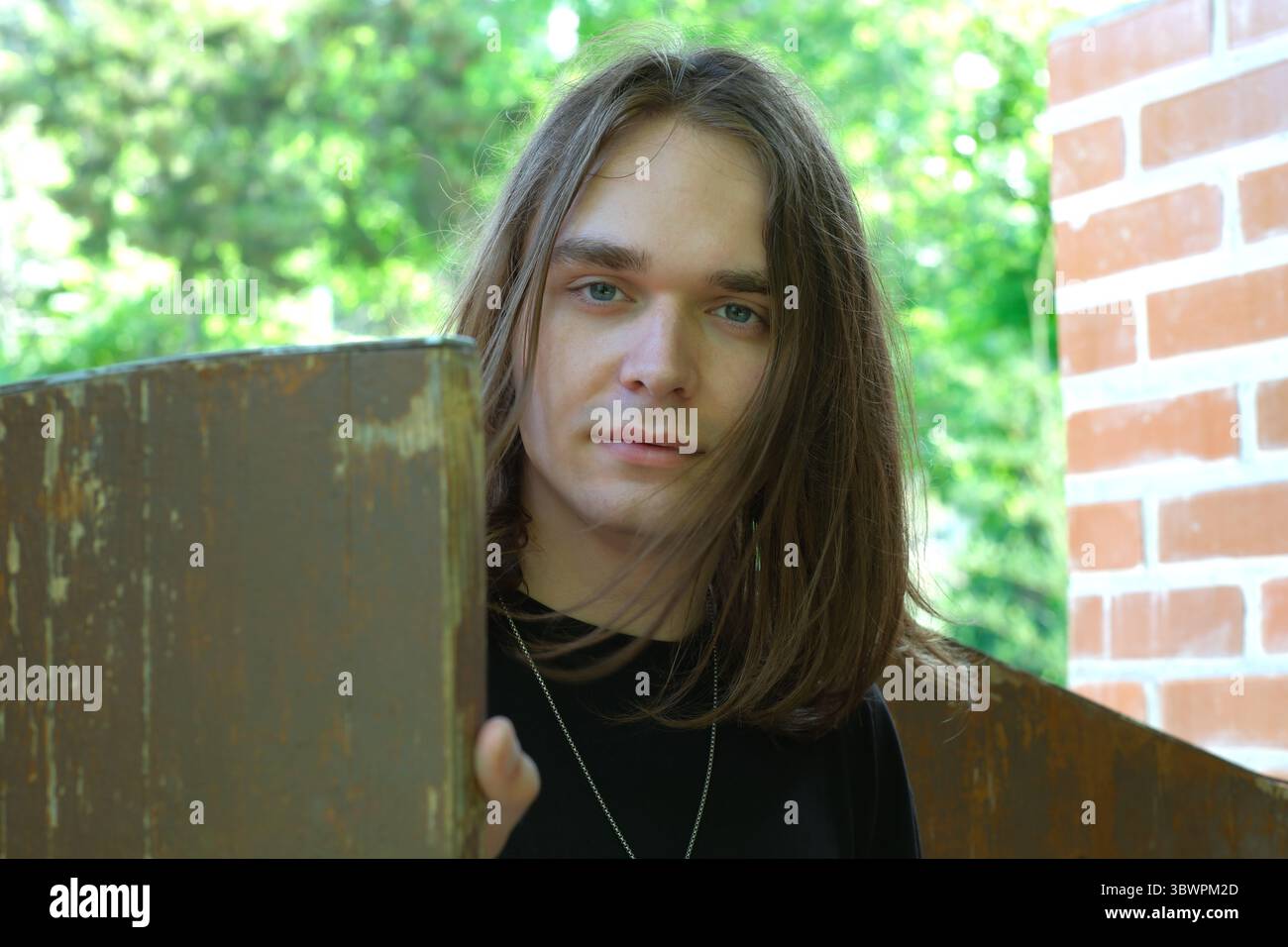 Un jeune homme s'appuie contre une structure en bois tout en souriant au soleil. Banque D'Images