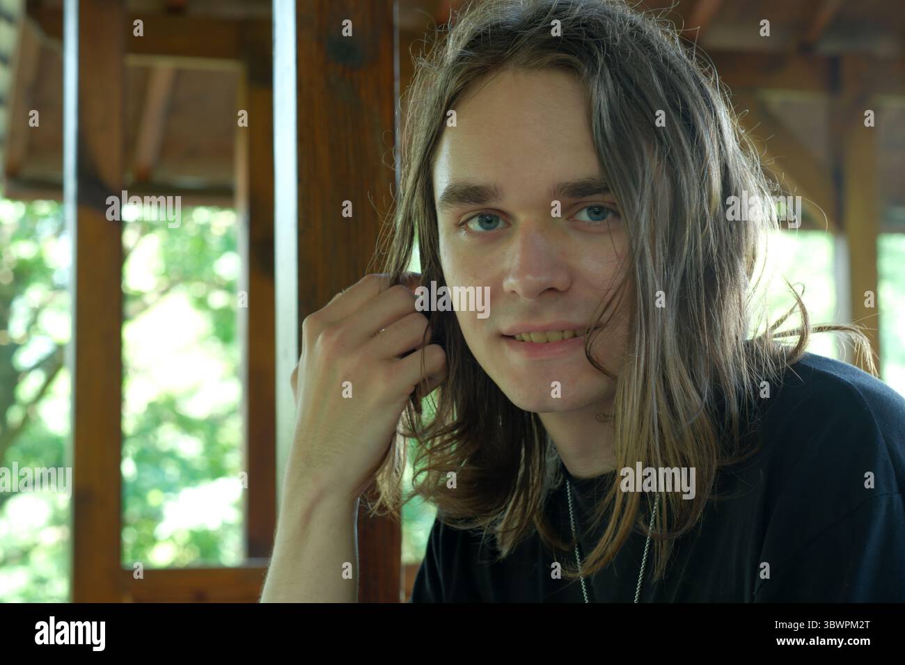 Un jeune homme aux cheveux longs se détend dans une structure en bois dans la nature. Banque D'Images