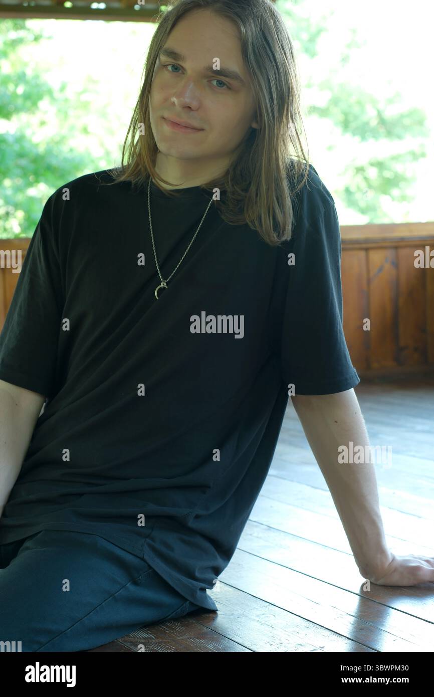Une jeune personne avec de longs cheveux s'assoit décontractée sur le sol, profitant de l'atmosphère calme. Banque D'Images