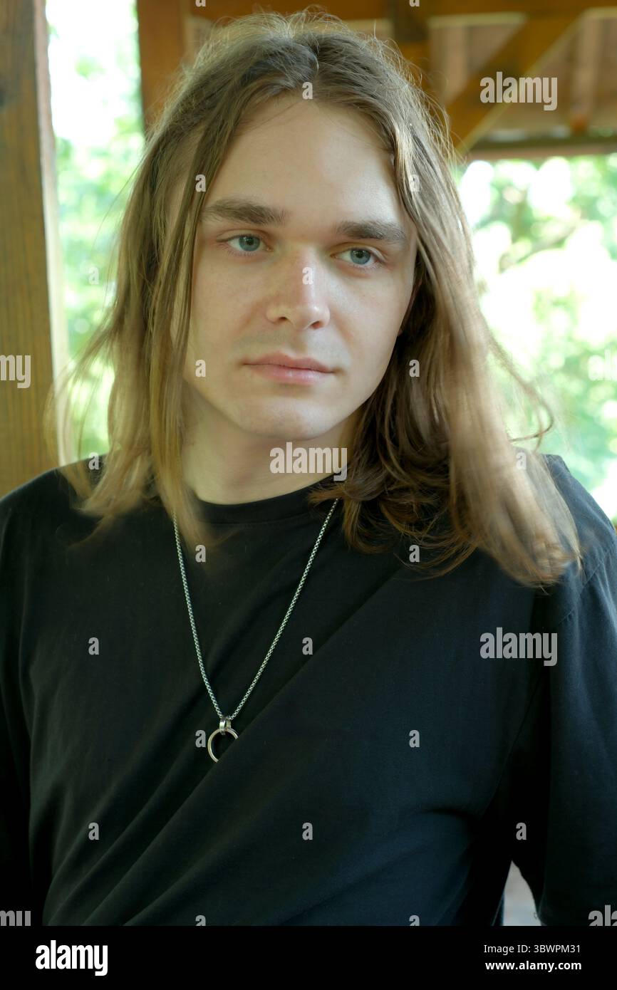 Un jeune homme aux cheveux longs se tient dans un espace ensoleillé, regardant soigneusement devant. Banque D'Images