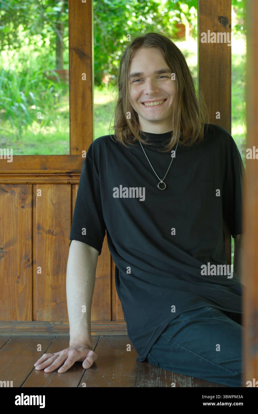 Un jeune homme joyeux s'assoit confortablement dans un belvédère rustique, profitant de la beauté de la nature. Banque D'Images