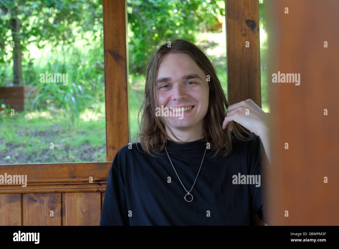 Un jeune homme se détend dans un gazebo en bois, souriant paisiblement tout en profitant de la nature. Banque D'Images