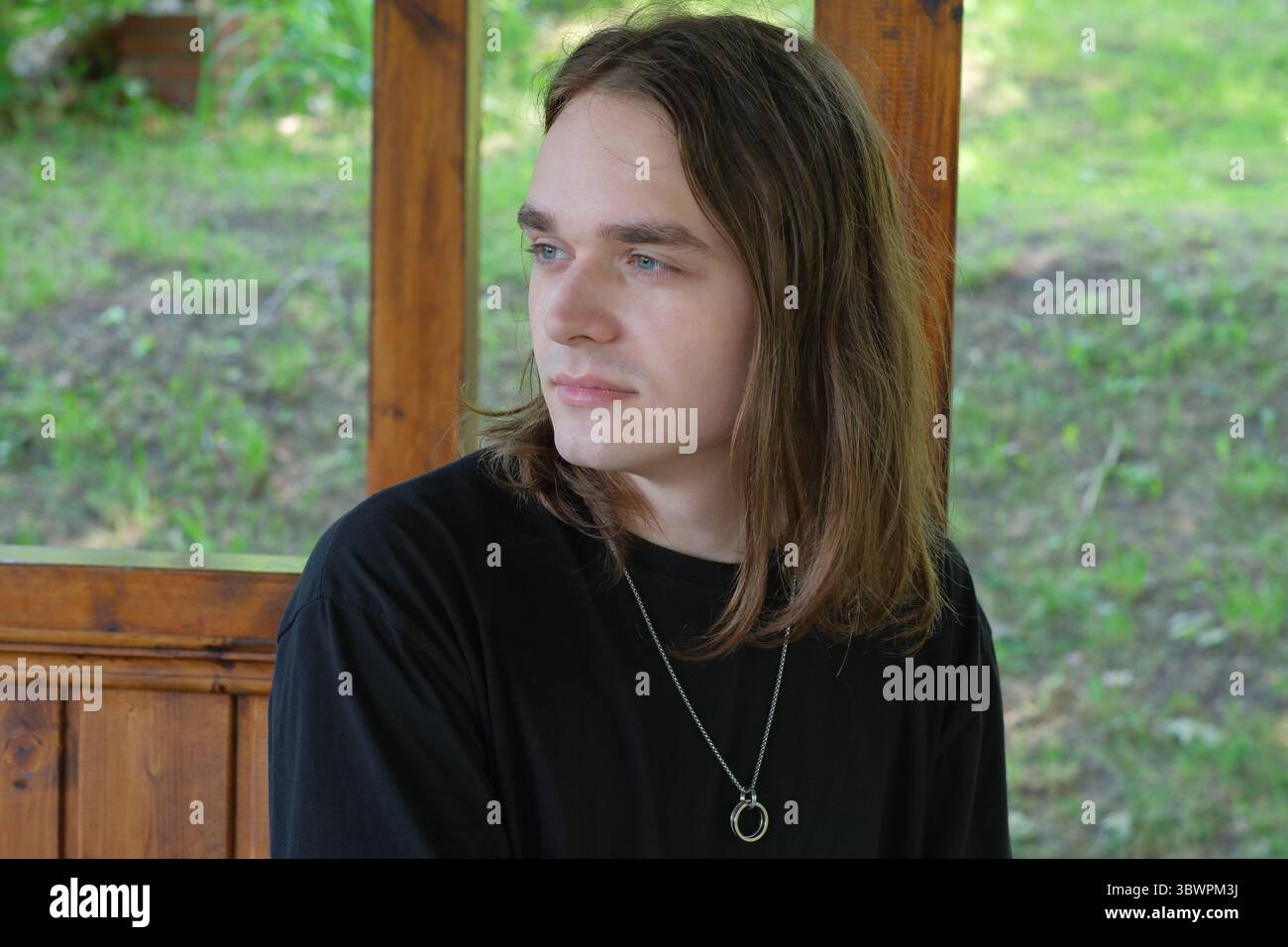 Un jeune homme est assis dans un belvédère en bois, perdu dans la pensée au milieu du calme de la nature. Banque D'Images