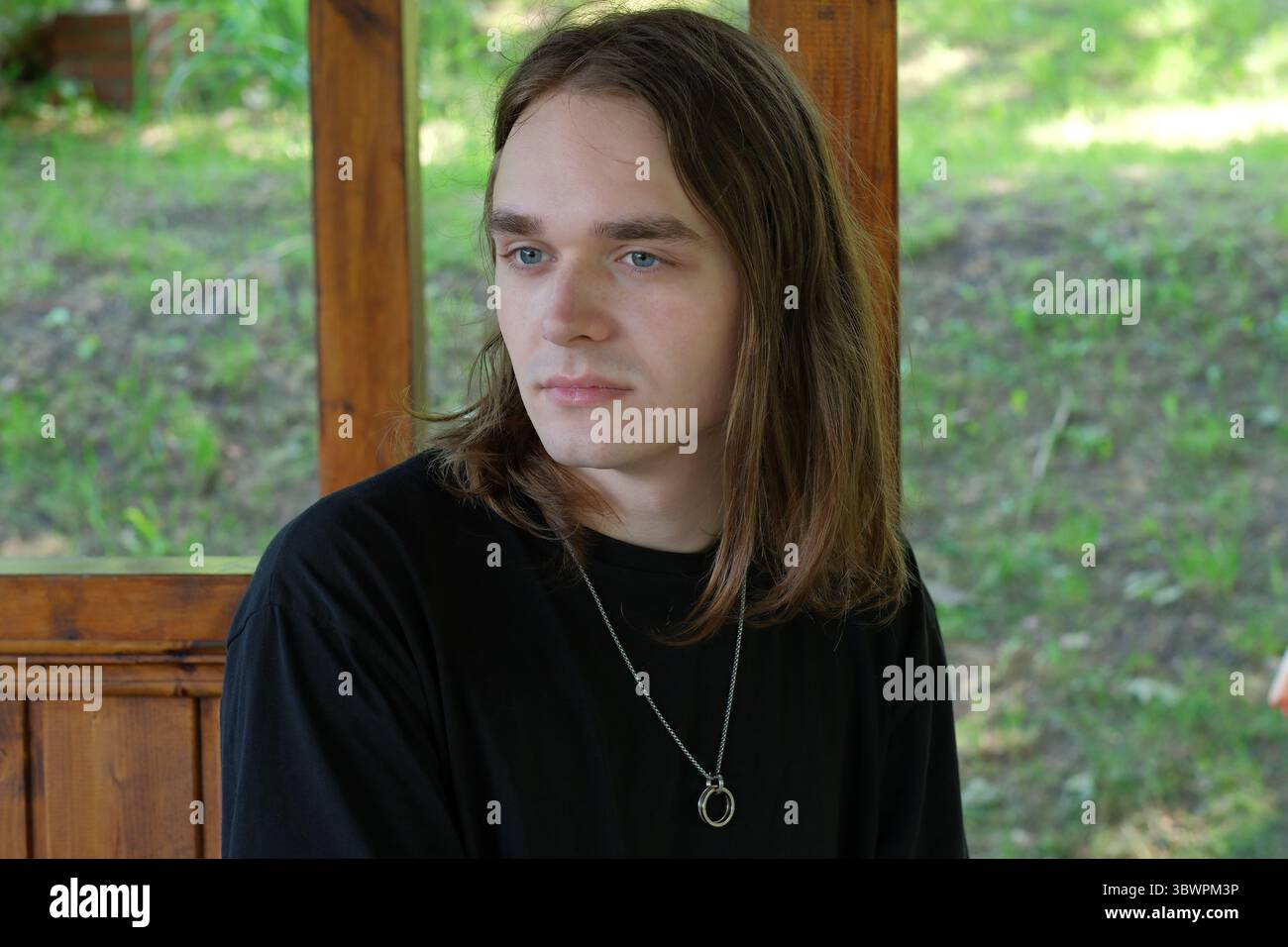 Une jeune personne aux cheveux longs est assise tranquillement dans un gazebo en bois, réfléchissant. Banque D'Images