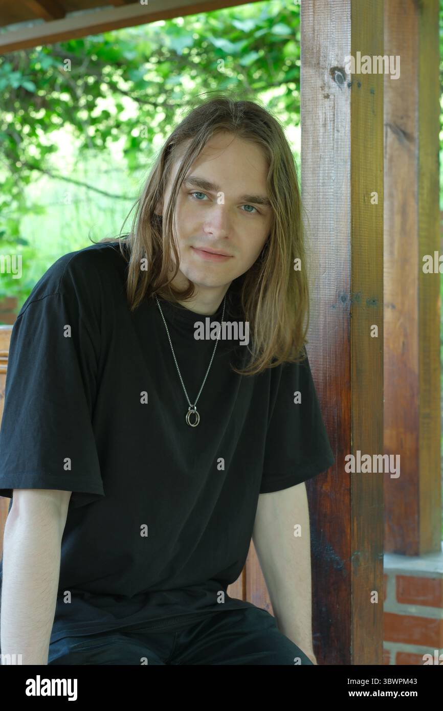 Une jeune personne aux cheveux longs pose soigneusement par des poutres en bois et de la verdure. Banque D'Images