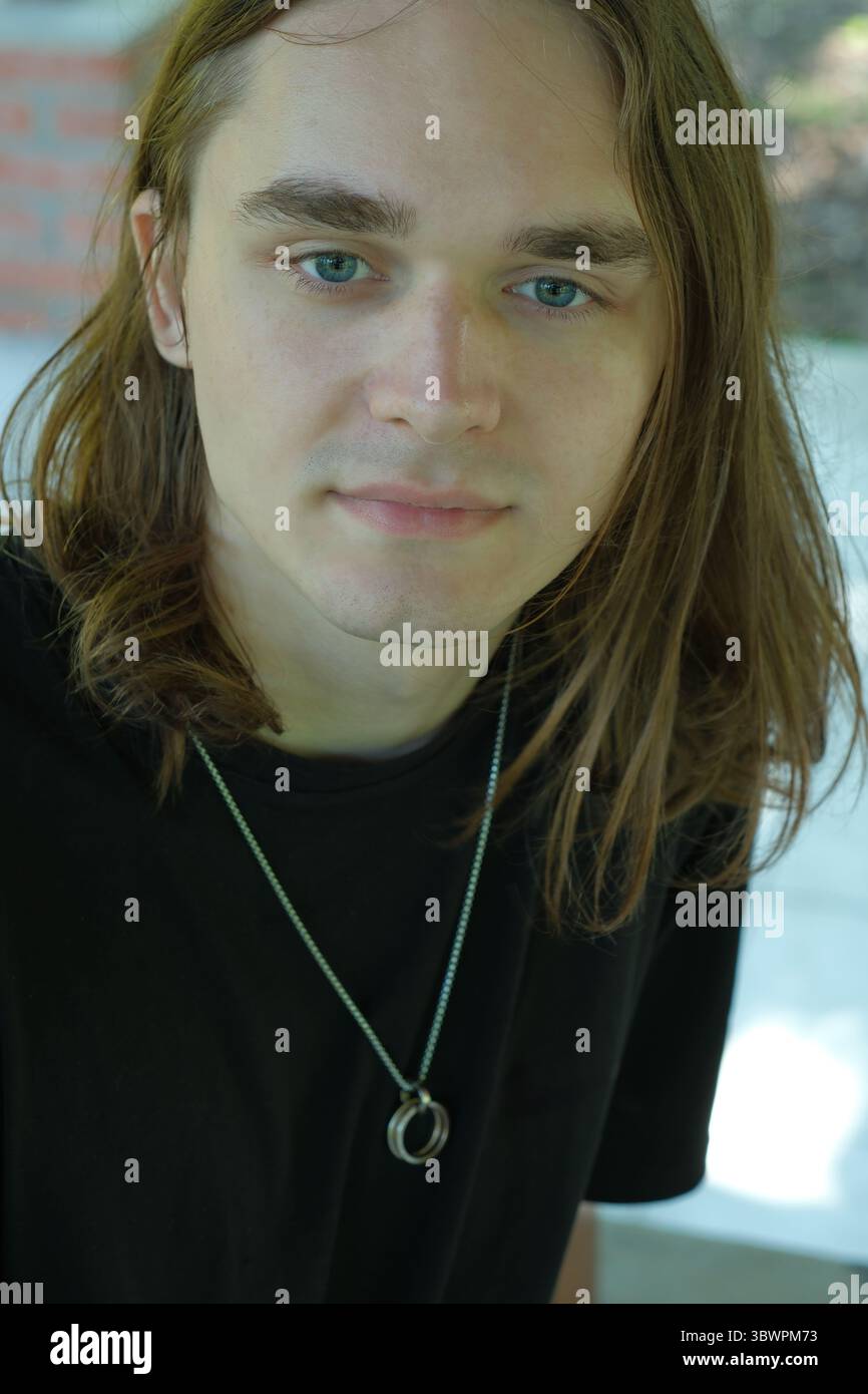 Un jeune homme contemplatif est assis à l'extérieur, entouré par la nature dans la lumière chaude du soleil. Banque D'Images