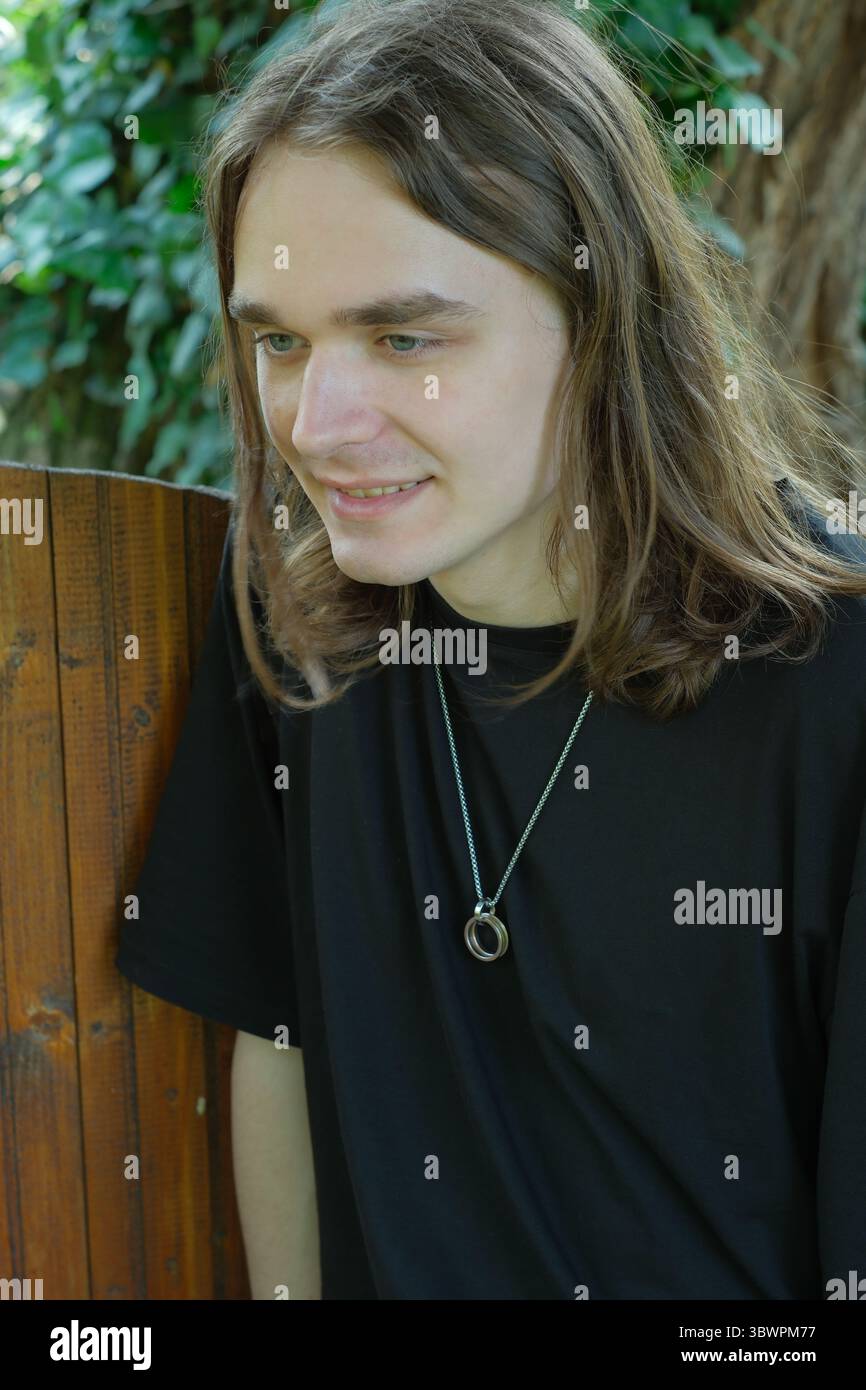 Un jeune homme sourit par une clôture en bois, entouré de verdure. Banque D'Images