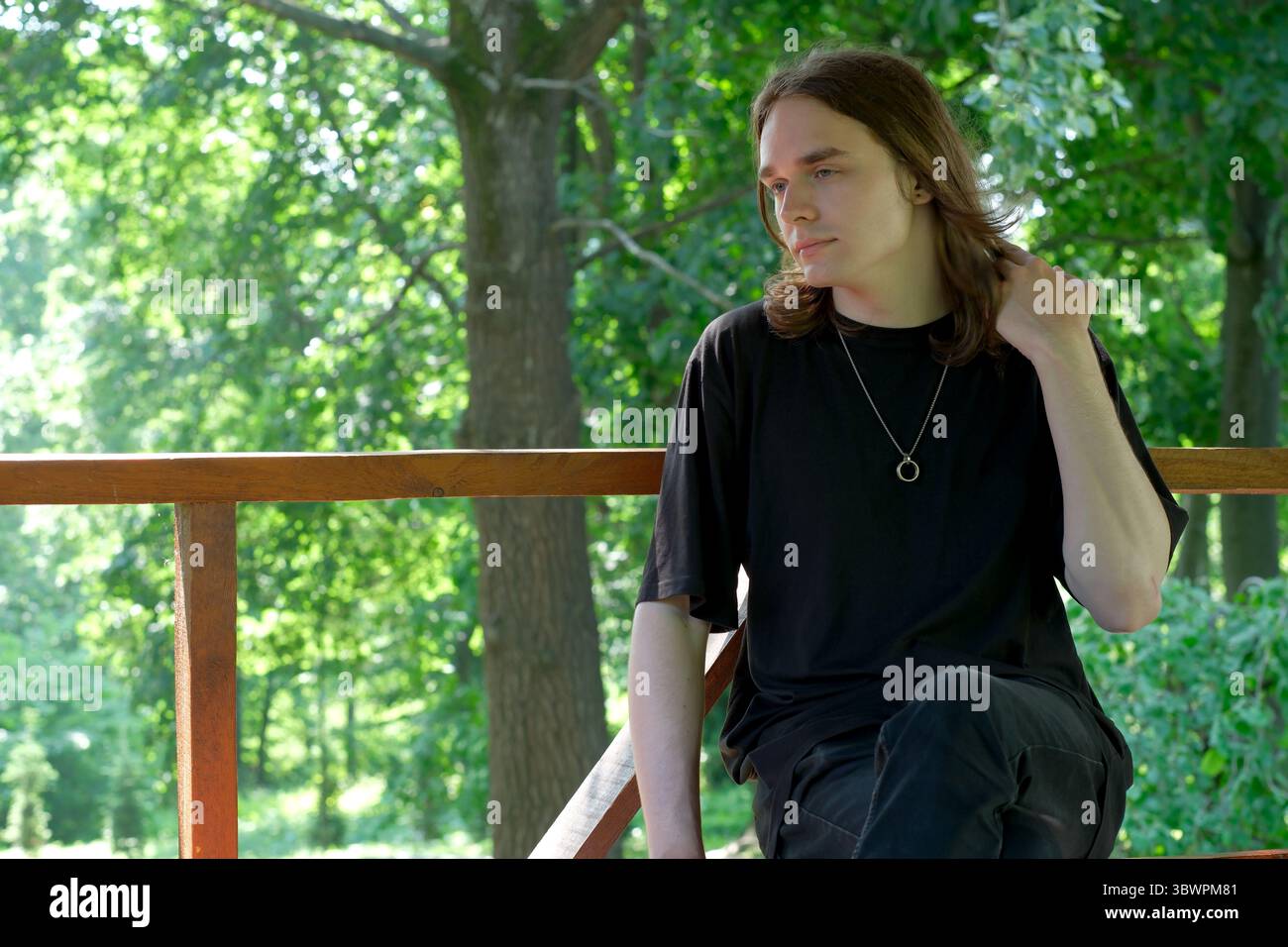 Assis sur une balustrade en bois, un jeune homme réfléchit au milieu d'une végétation luxuriante. Banque D'Images