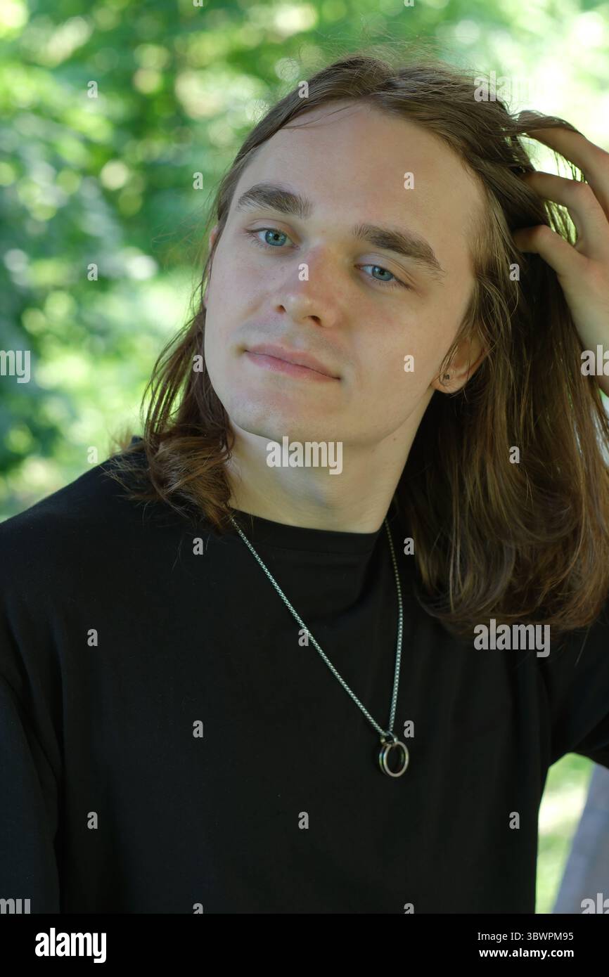 Un jeune homme aux cheveux longs s'arrête dans un environnement verdoyant luxuriant, perdu dans ses pensées. Banque D'Images