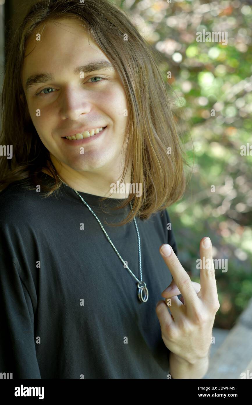 Un homme joyeux se tient dehors, souriant brillamment tout en faisant un signe de paix. Banque D'Images