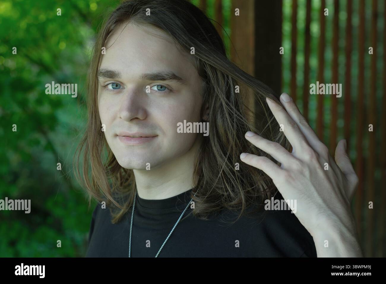 Un jeune homme se tient debout dans un cadre verdoyant, touchant ludique ses cheveux à la douce lumière du soleil. Banque D'Images