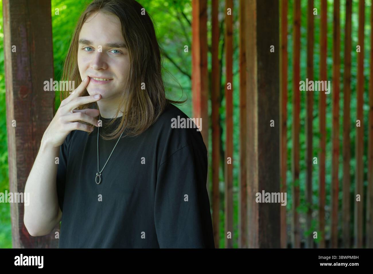 Un jeune homme réfléchi se tient sous une structure en bois, entouré d'une végétation luxuriante. Banque D'Images