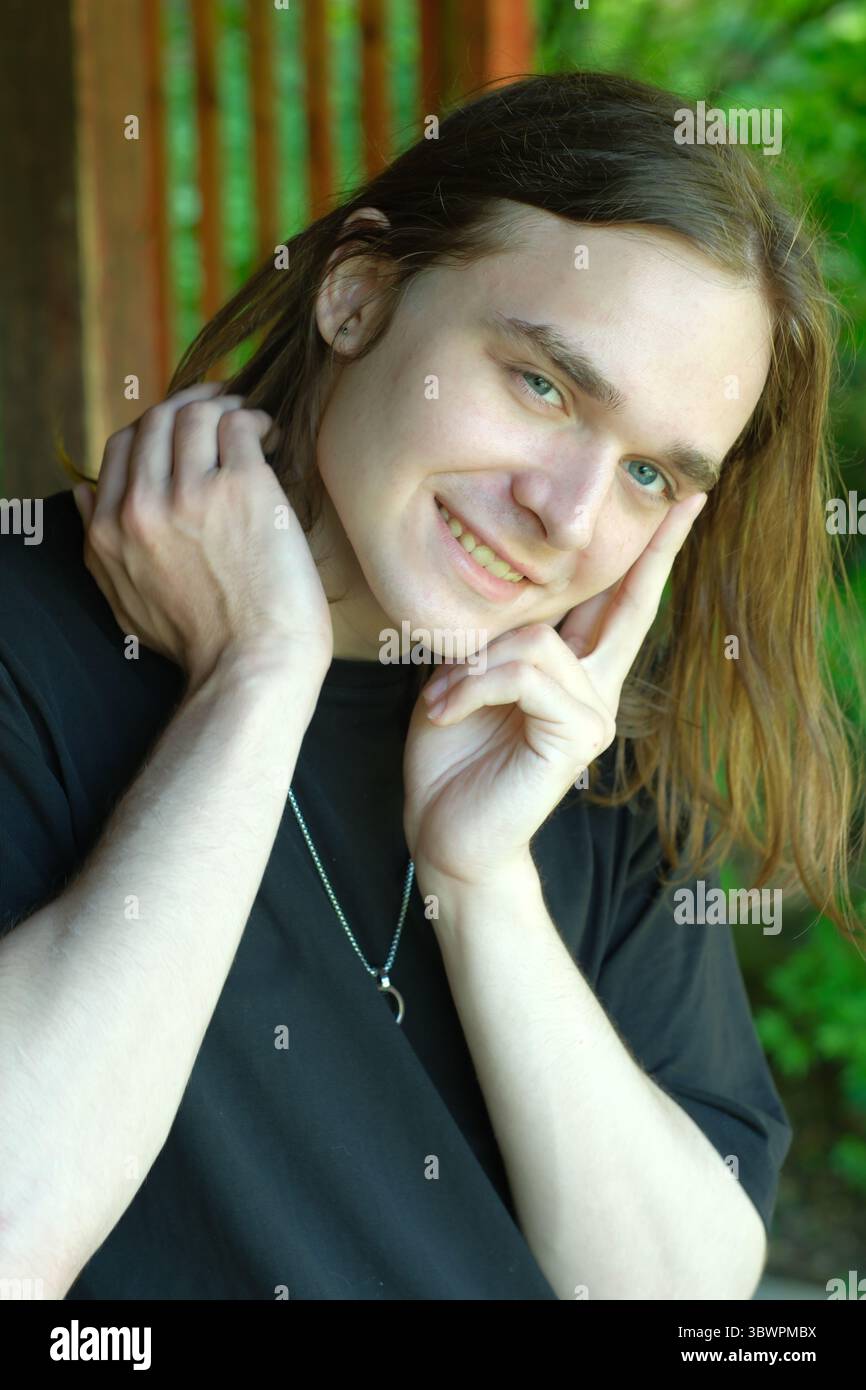 Un jeune homme se tient dehors, présentant un sourire charmant au milieu d'une végétation luxuriante. Banque D'Images