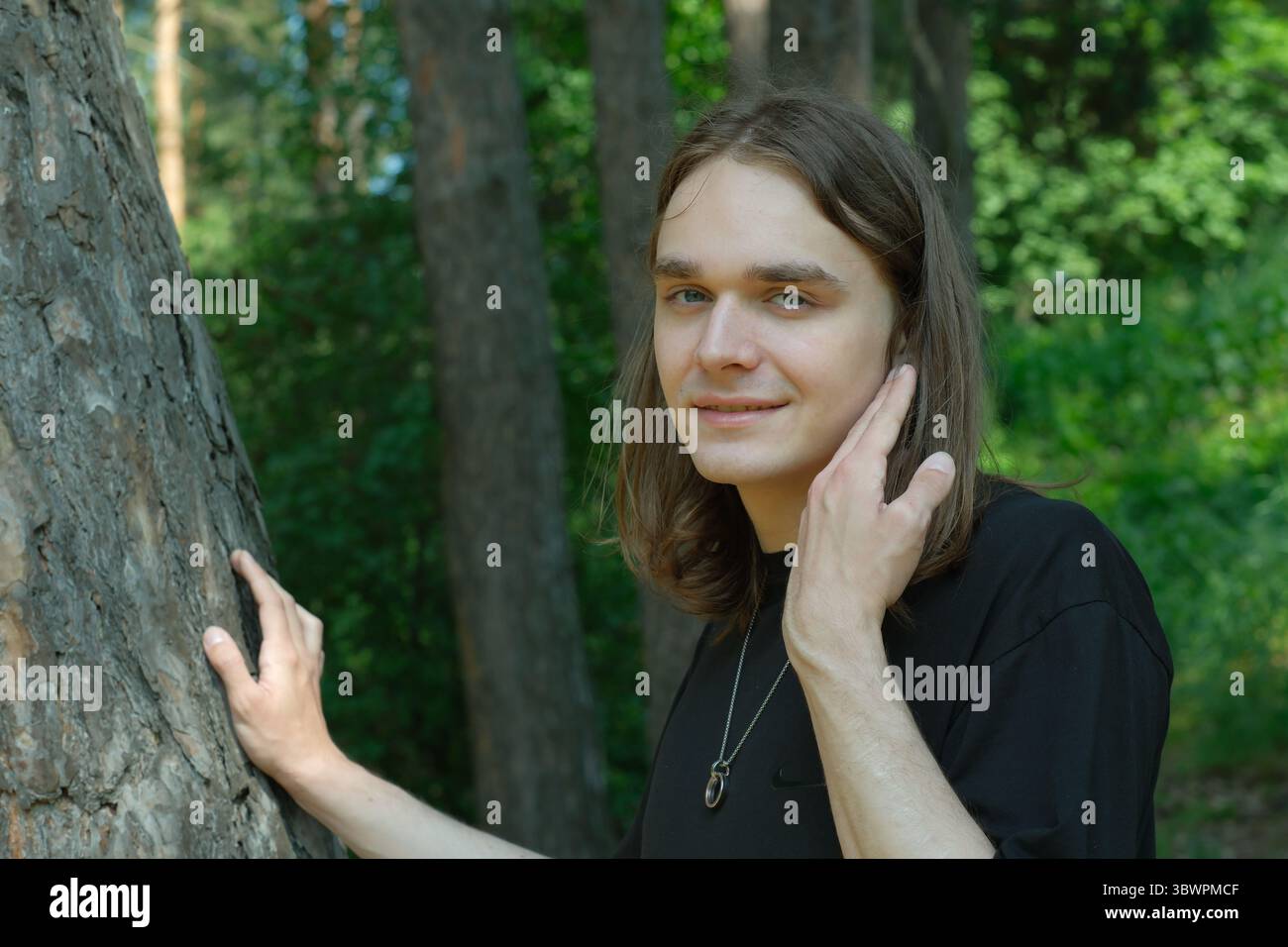 Un jeune individu se tient doucement près d'un grand arbre, profitant de l'environnement serein de la forêt. Banque D'Images
