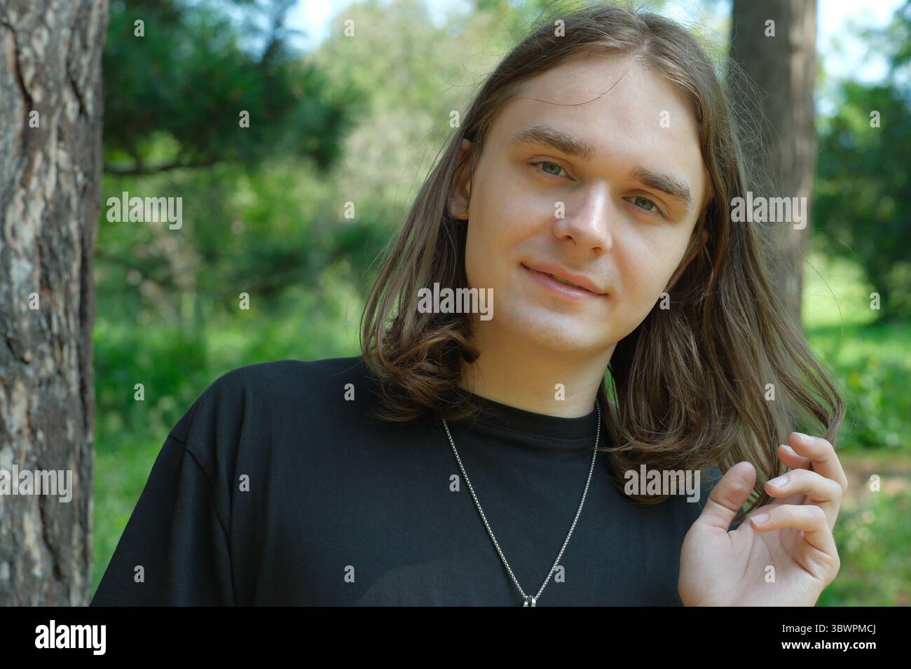 Une jeune personne se tient à côté d'un arbre, souriant doucement tout en profitant de l'extérieur serein. Banque D'Images
