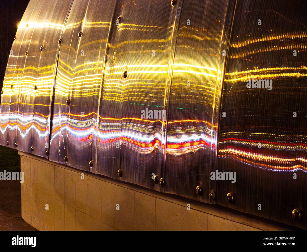 Traînées de lumière se reflétant sur les feuilles de plastique polycarbonate créant un motif abstrait et coloré la nuit Banque D'Images