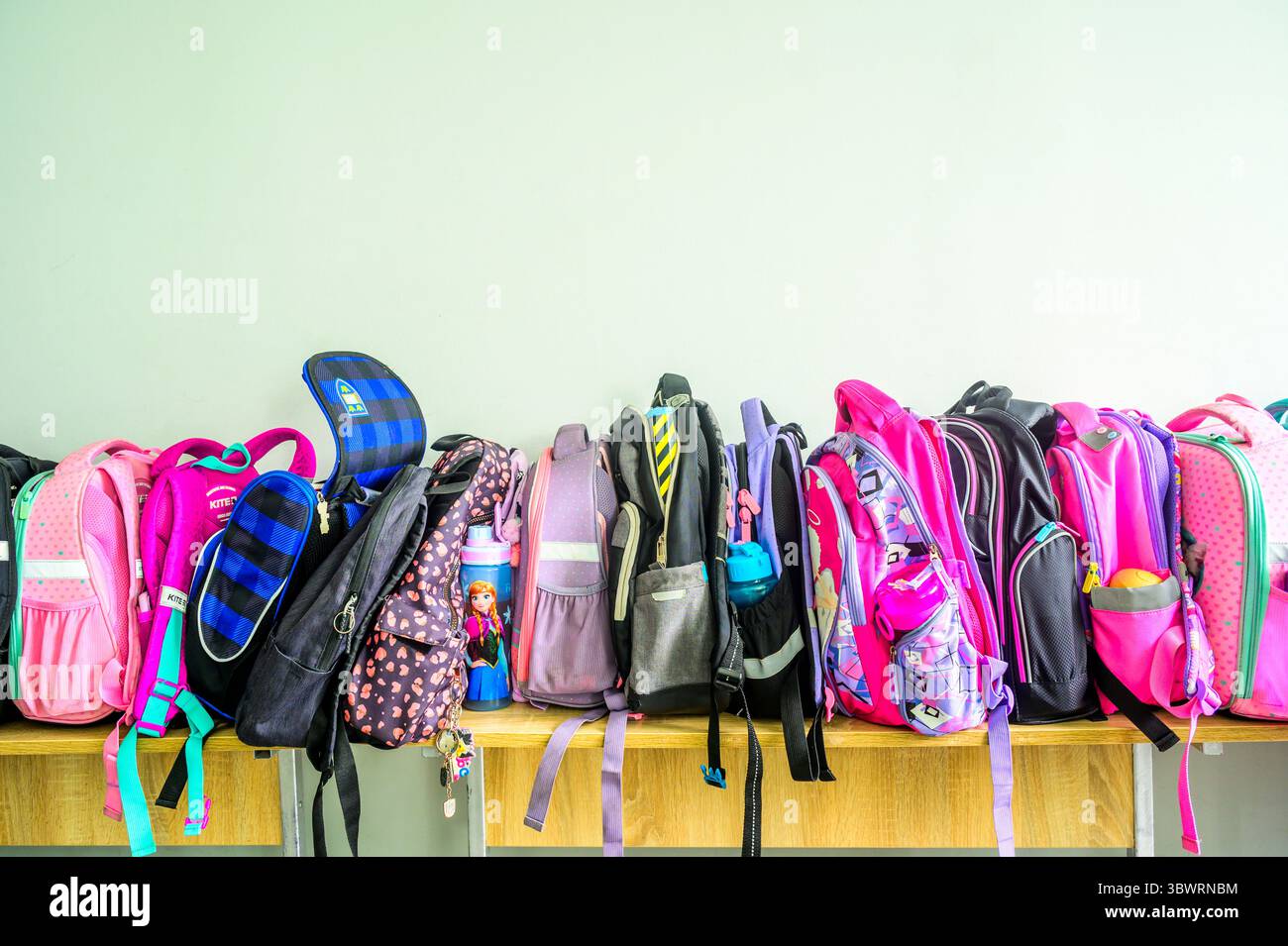Sacs à dos d'école colorés suspendus à des crochets et reposant sur un banc en bois dans une salle de classe vide, prêts pour les étudiants avides et l'apprentissage Banque D'Images
