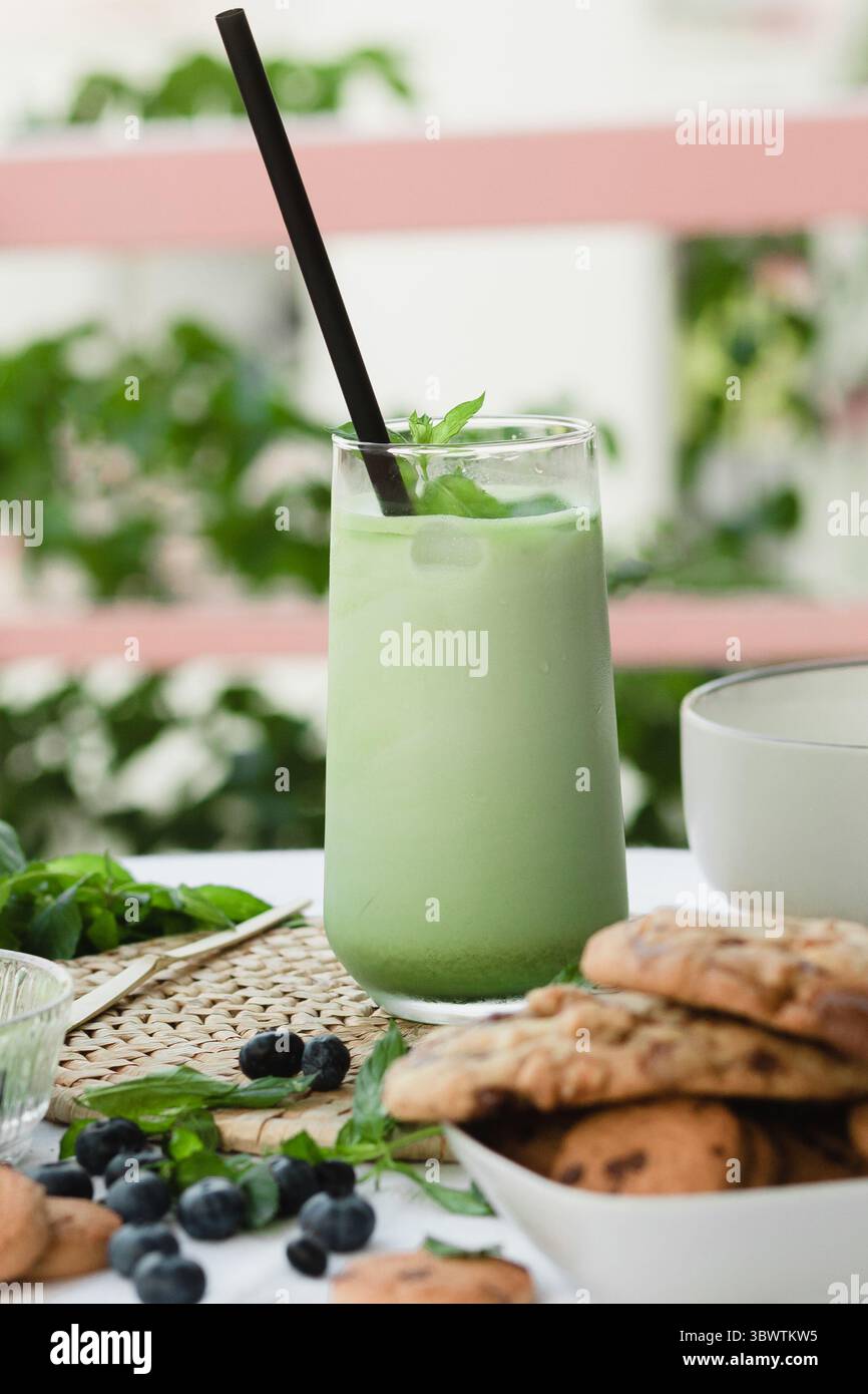 Latte matcha glacé sur un tapis tissé naturel avec de la menthe, des baies et des biscuits. Boisson esthétique pour une vie soucieuse de la santé. Plan publicitaire vertical Banque D'Images