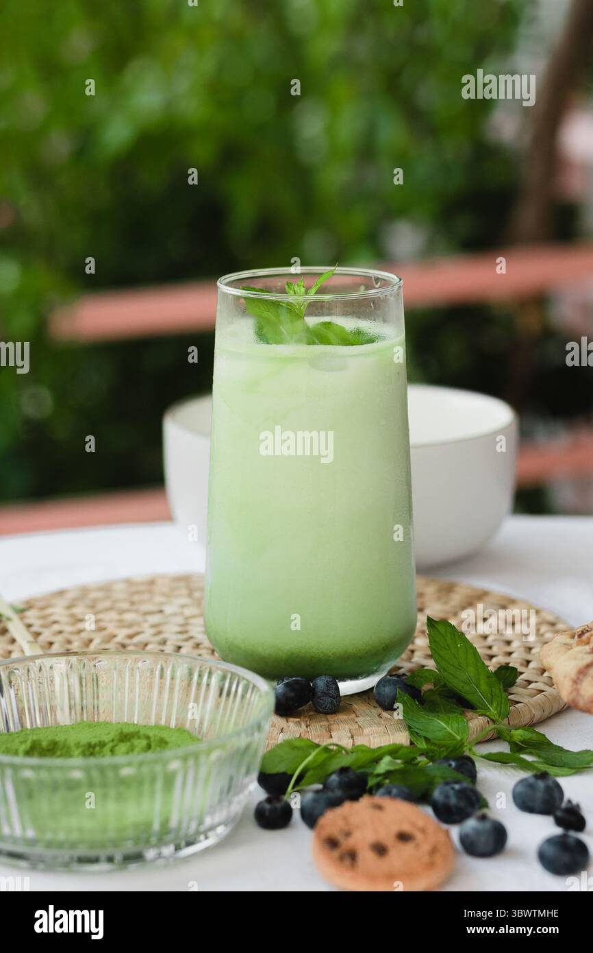Latte matcha glacé sur un tapis tissé naturel avec de la menthe, des baies et des biscuits. Boisson esthétique pour une vie soucieuse de la santé. Plan publicitaire vertical Banque D'Images