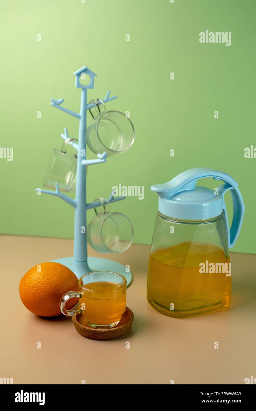 Un ensemble de tasses en verre sur un support bleu clair avec un pichet de jus d'orange frais. Petit déjeuner et concept de rafraîchissement sain sur un fond bicolore. Banque D'Images