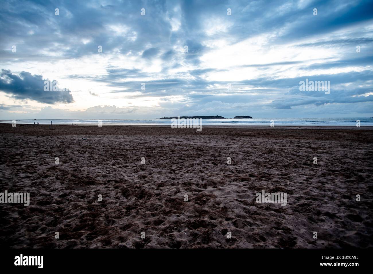 Coucher de soleil sur les vastes plages d’Essaouira avec un ciel bleu, des nuages blancs et des vagues s’écrasant sur le rivage au Maroc Banque D'Images