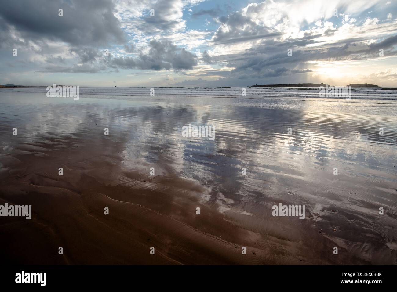 Coucher de soleil sur les vastes plages d’Essaouira avec un ciel bleu, des nuages blancs et des vagues s’écrasant sur le rivage au Maroc Banque D'Images