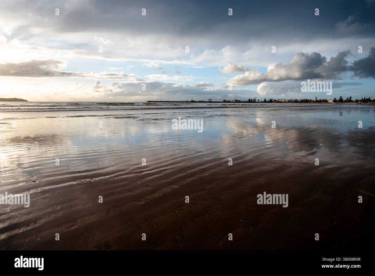 Coucher de soleil sur les vastes plages d’Essaouira avec un ciel bleu, des nuages blancs et des vagues s’écrasant sur le rivage au Maroc Banque D'Images