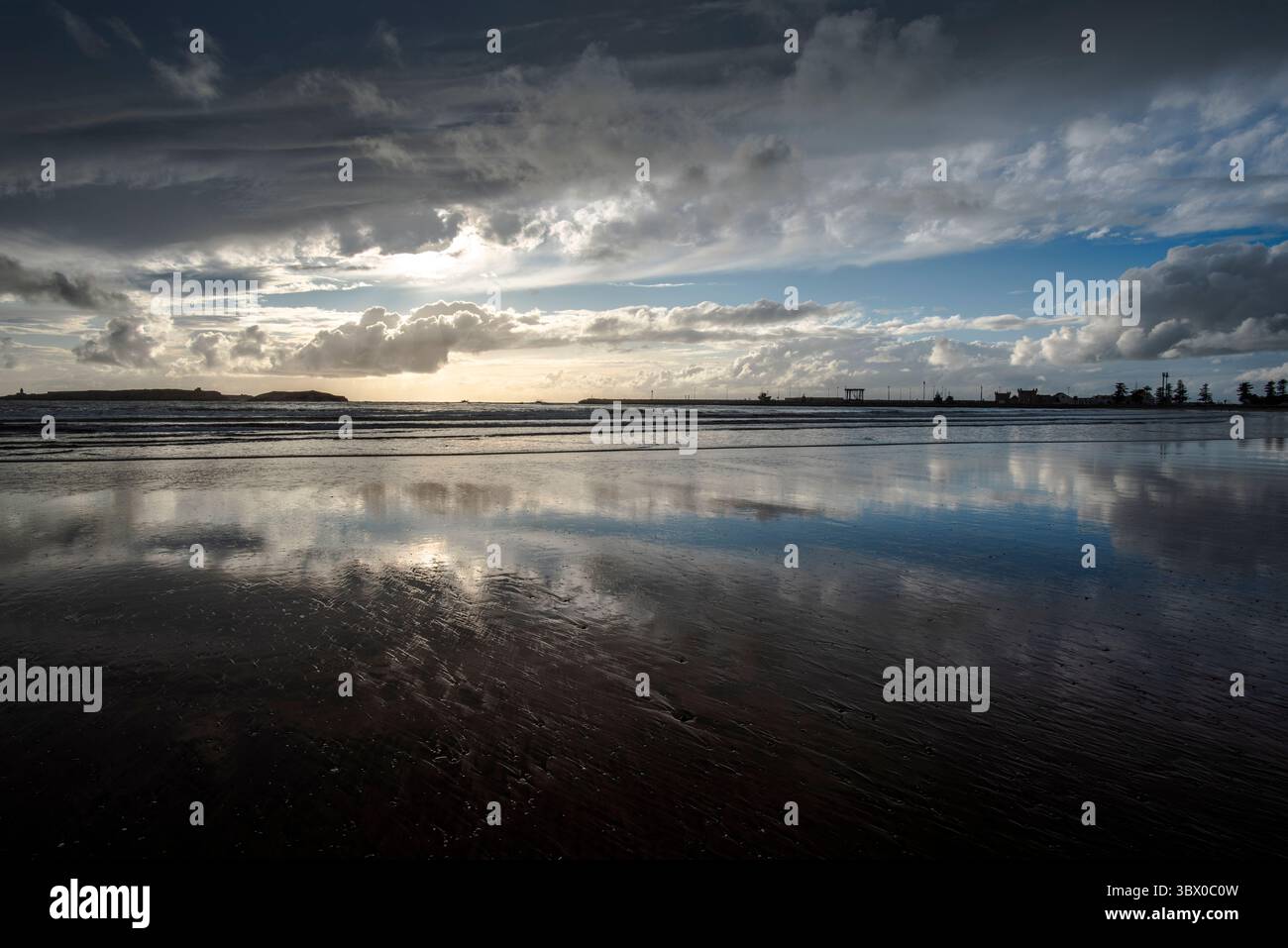 Coucher de soleil sur les vastes plages d’Essaouira avec un ciel bleu, des nuages blancs et des vagues s’écrasant sur le rivage au Maroc Banque D'Images