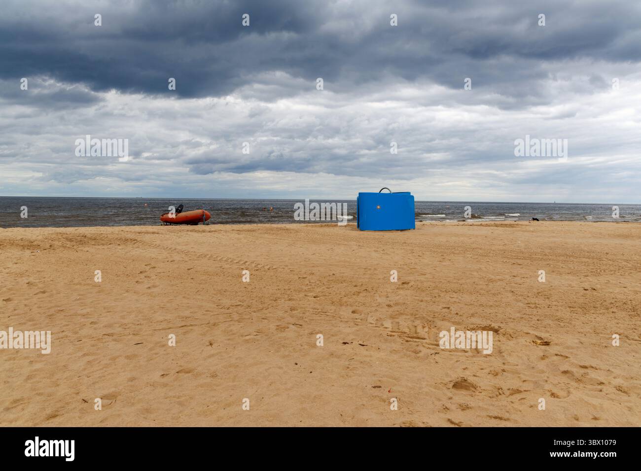 Un stand bleu de sauveteur et un bateau gonflable sont assis sur une large plage de sable sous un ciel nuageux spectaculaire, près de la mer Baltique calme. Banque D'Images