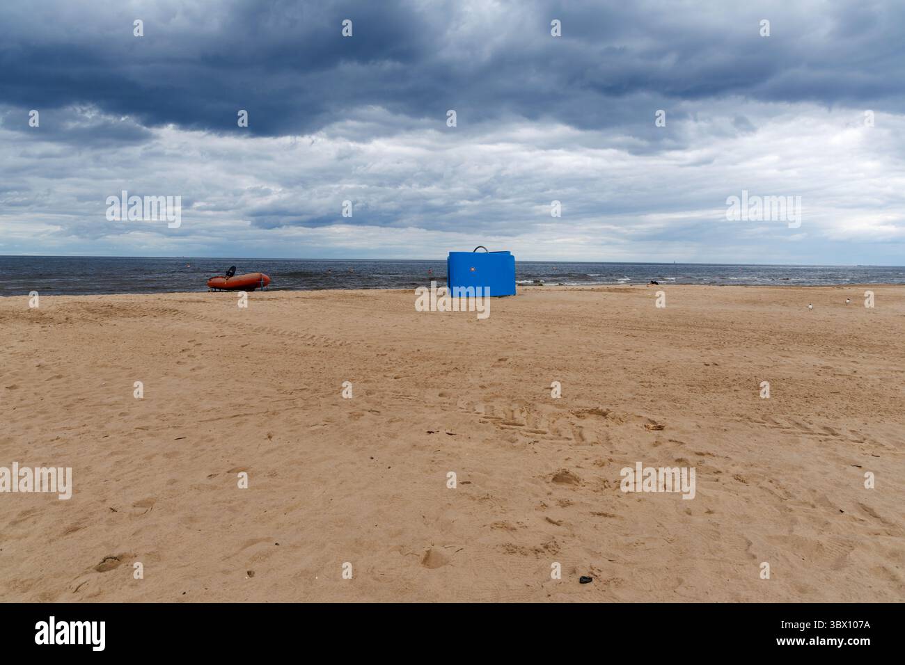 Un stand bleu de sauveteur et un bateau gonflable sont assis sur une large plage de sable sous un ciel nuageux spectaculaire, près de la mer Baltique calme. Banque D'Images