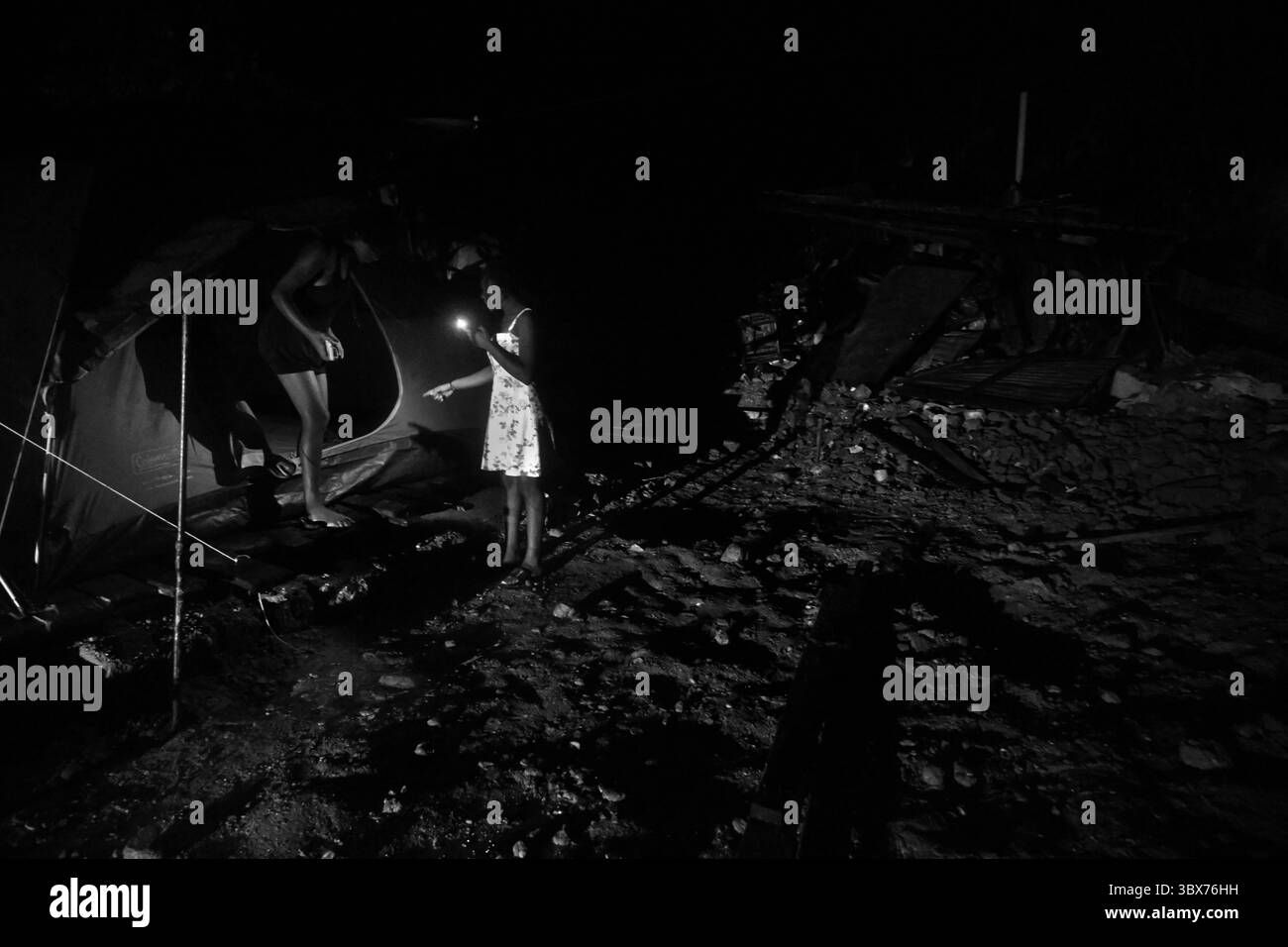 25 août 2021, Maniche, Haïti : S’il y a de la vie, il y a hopeâ€™ â€“ Chrislome Lorbensky, survivant..Un voisin se tient dans l’obscurité sans pouvoir. puissance alors qu'ils dressent des tentes. Chrislome Lorbensky et son épouse Altema Rosenine avec leur fils de 11 mois Adonia Ande Lorbensky, surnommé ton ton font face aux conséquences d'un ouragan massif à Maniche, Haïti le 25 août 2021. ..ils ont perdu leur fille de 3 ans dans le séisme et se sont accrochés à leur bébé survivant avec un plâtre sur sa jambe cassée. Il a été retrouvé sous le cadavre de son oncle sur ce terrain où ils s'efforcent maintenant de reconstruire. Ils ont dû quic Banque D'Images