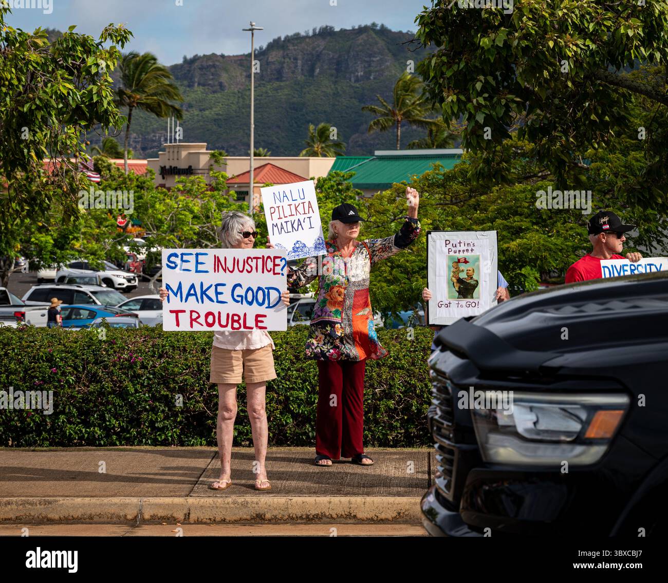 Un manifestant agite un "voir injustice ? Signe « faire bon trouble » chez les automobilistes à côté d'une femme avec un signe « faire bon trouble » hawaïen signe un rassemblement au Kukui Banque D'Images