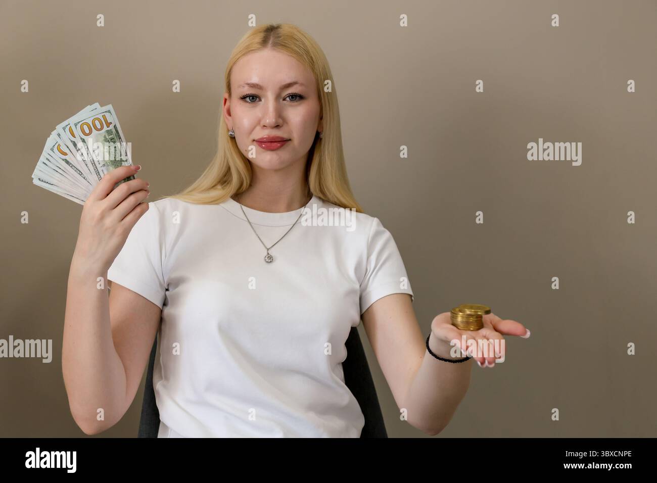 Femme blonde dans un t-shirt blanc tenant des billets de dollars américains dans une main et une pile de bitcoins d'or dans l'autre, symbolisant le choix entre traditio Banque D'Images
