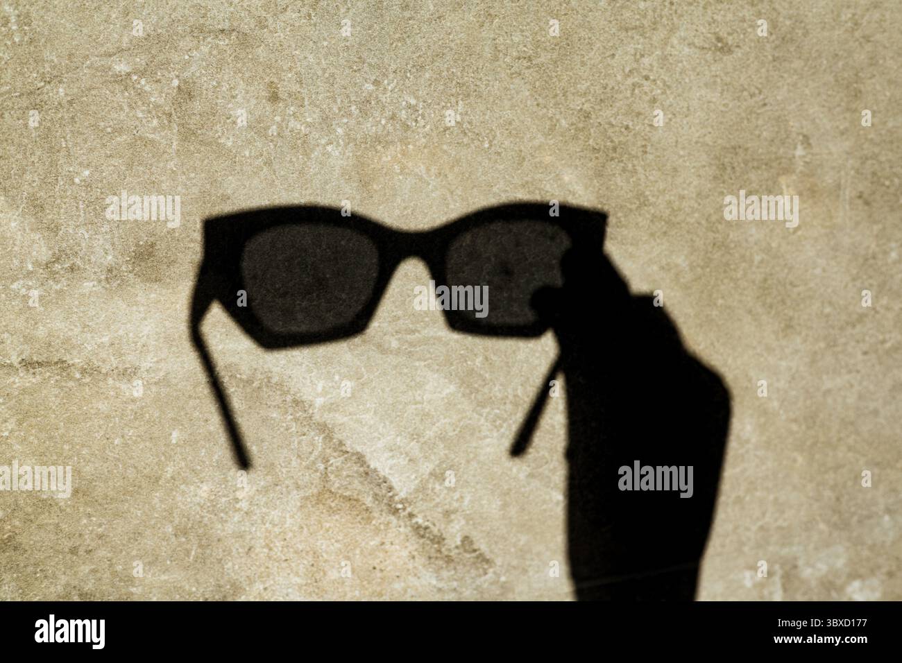 L'ombre des lunettes de soleil, projetée sur un mur texturé, crée une image unique et élégante. Une ombre de lunettes de soleil est projetée sur une surface texturée, showcasin Banque D'Images