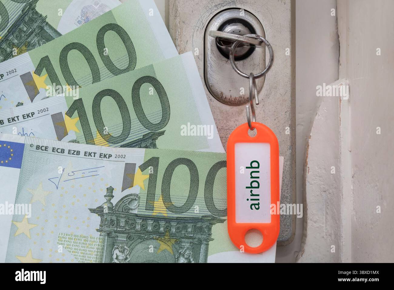 Une clé est coincée dans la serrure de la porte, les mots Airbnb sont gravés sur l'étiquette et il y a des billets en euros à côté. Banque D'Images