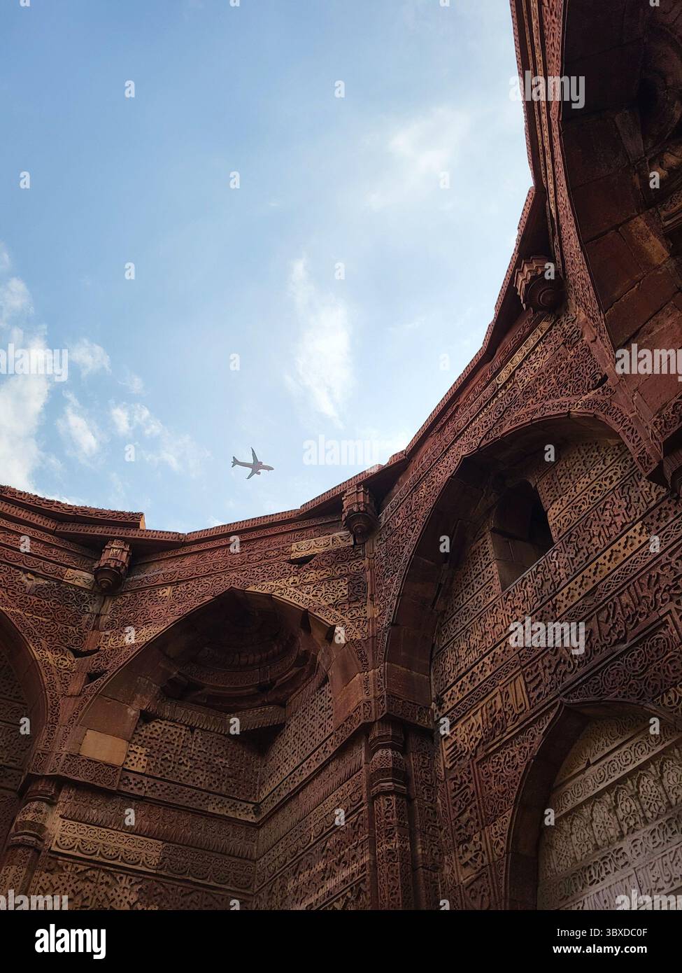 Arches mogholes historiques à Qutub Minar, Delhi, avec avion traversant le ciel. - Image de stock capturée avec un smartphone