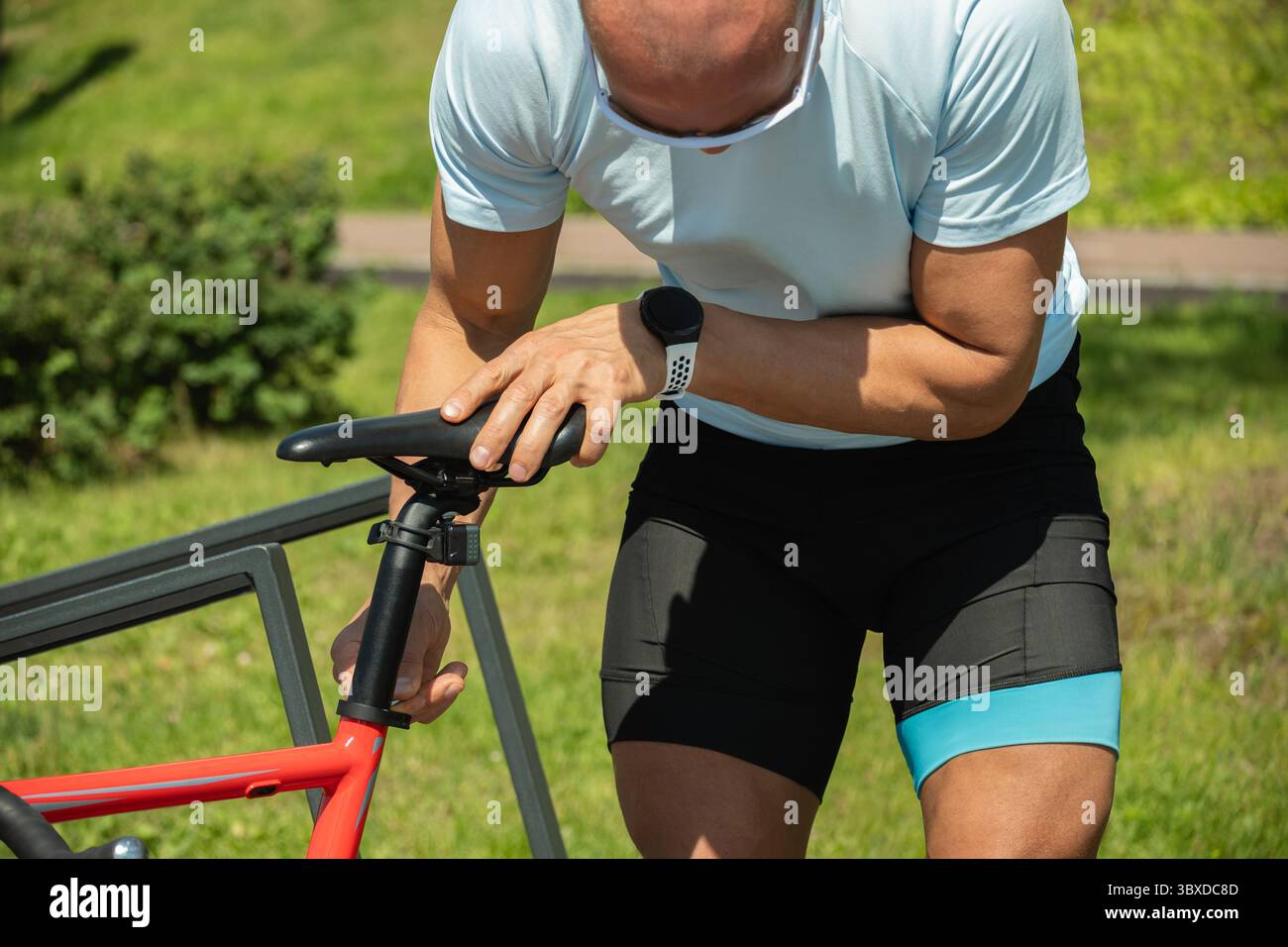 Homme ajustant la selle de vélo avec l'outil de clé hexagonale dans le parc public nature. Activité estivale. Banque D'Images