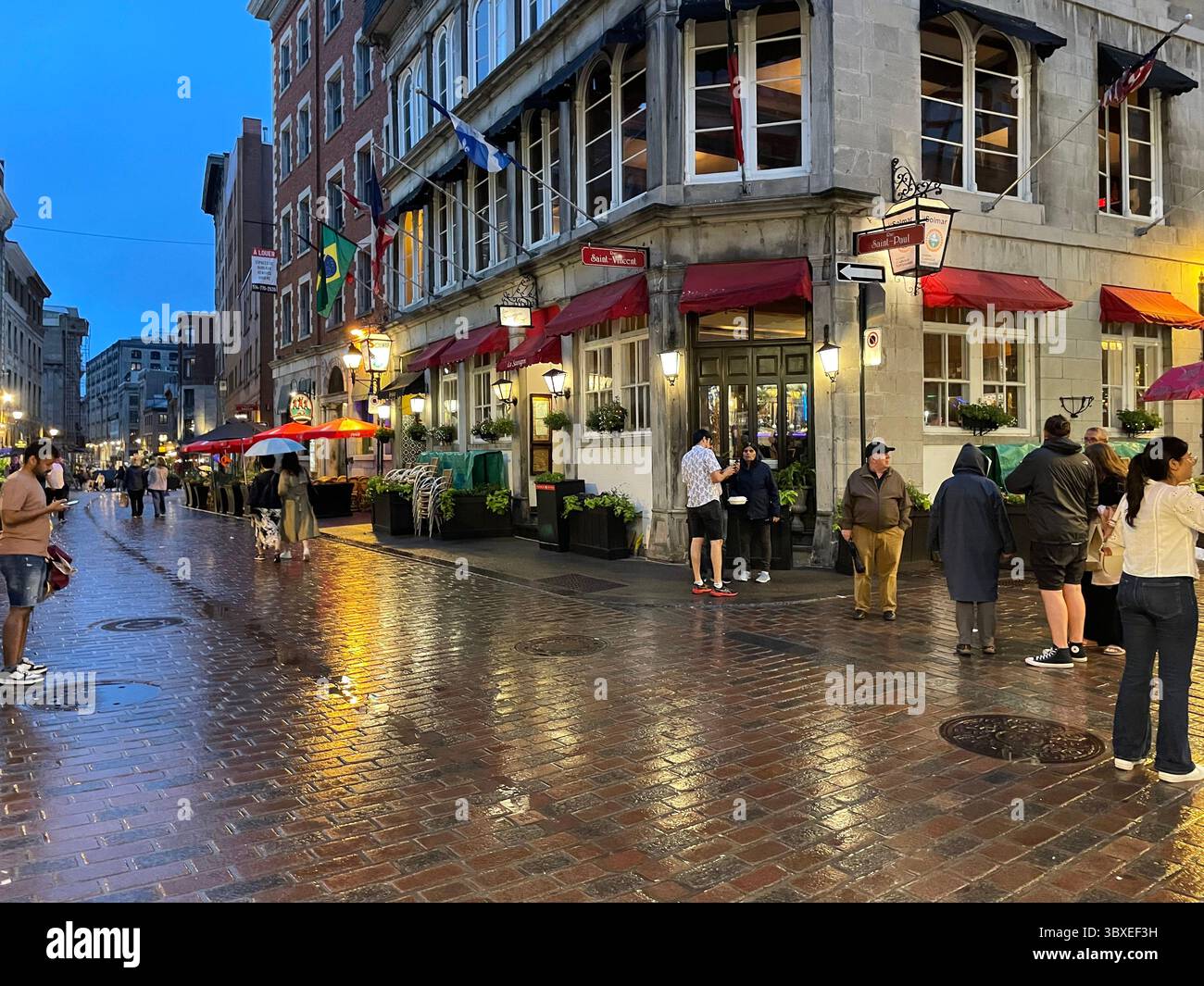 Une petite foule de gens profitent d’une soirée d’été pluvieuse dans le Vieux-Montréal, en dégustant les cafés, bistrots et boutiques du quartier historique de la ville Banque D'Images