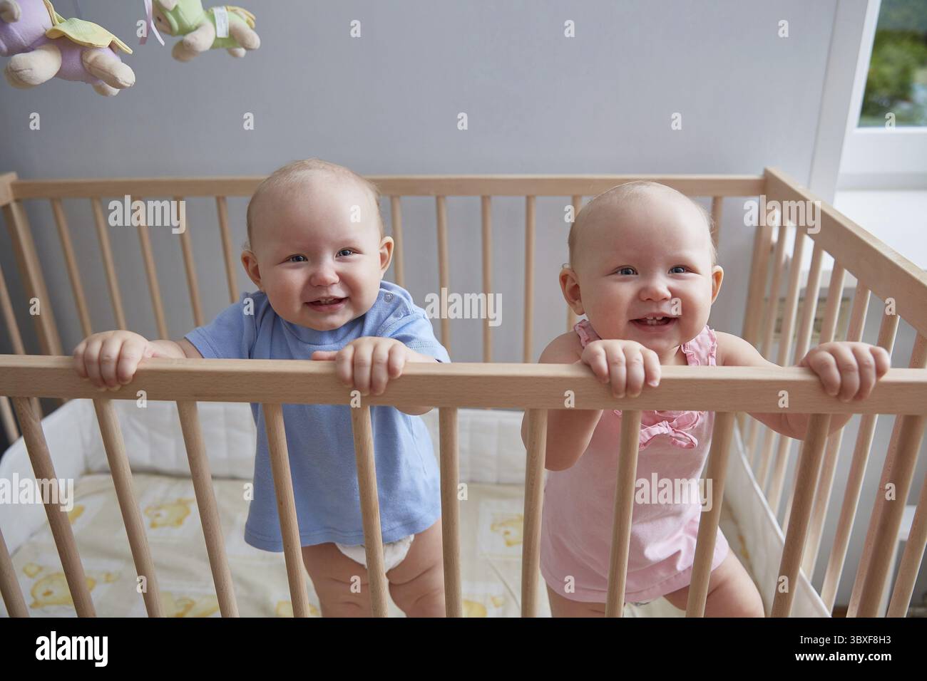 Les enfants jumeaux, garçon et fille, sourient en se tenant debout le berceau Banque D'Images