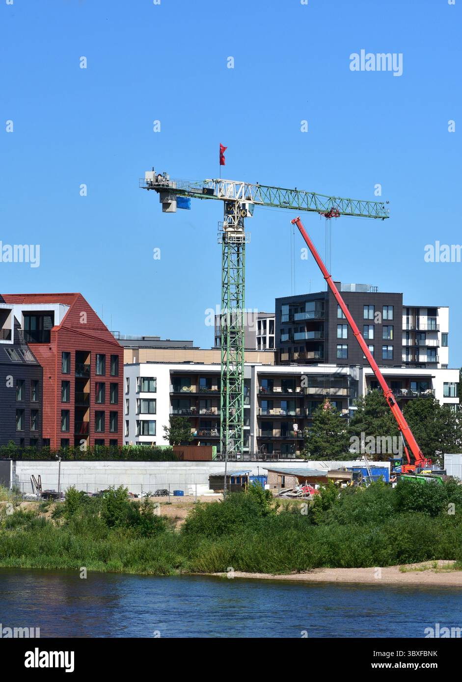 Grues et chantier de construction dans le quartier moderne de la ville. Les immeubles d'appartements s'élèvent derrière les machines sous un ciel bleu clair. Croissance urbaine, développement et R Banque D'Images