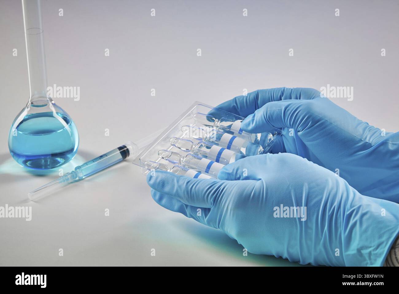 Mains dans des gants jetables contenant un jeu de cinq ampoules de liquide. Flacon médical avec réactif chimique bleu, seringue isolée sur blanc. Laboratoire r Banque D'Images